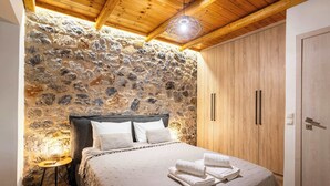 A bedroom with a stone wall, wooden ceiling, a bed with white linens, and a wooden wardrobe. - Verga Paradise Nest - A Blissful Hideout (Paralia Vergas)