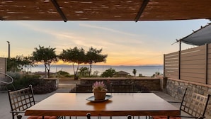 An outdoor patio with a wooden table and chairs, a potted plant, and a view of the sea at sunset. - Verga Paradise Nest - A Blissful Hideout (Paralia Vergas)