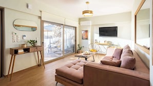 A modern living room with a sofa, a coffee table, a desk with a mirror, and a TV. - Verga Paradise Nest - A Blissful Hideout (Paralia Vergas)