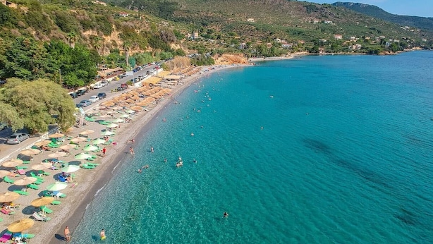 A coastal beach with clear turquoise water, umbrellas, and people swimming. - Verga Paradise Nest - A Blissful Hideout (Paralia Vergas)