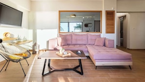 A modern living room with a sectional sofa, a coffee table, a wicker chair, and a flat-screen TV mounted on the wall. - Verga Paradise Nest - A Blissful Hideout (Paralia Vergas)