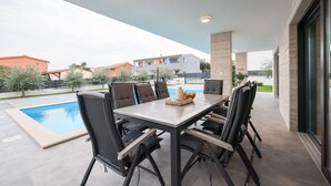 An outdoor patio with a pool, a dining table with chairs, and a view of neighboring buildings. - Luxury villa Marko, family-friendly and pet-friendly modern villa near sea.

 (Vir)