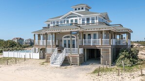 Una casa sulla spiaggia con un balcone, un portico coperto e una scala che conduce all'ingresso.