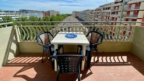 Un balcon avec une table et des chaises, donnant sur une rangée d’immeubles.