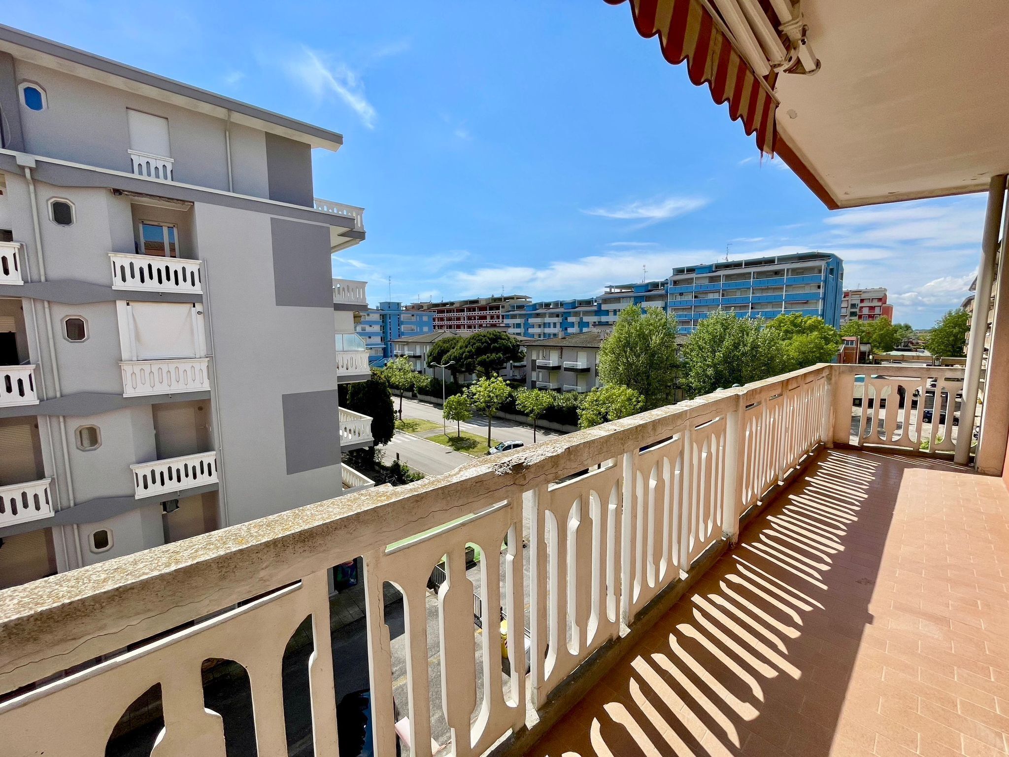A balcony with a view of multi-story buildings, a clear sky, and a street with trees.