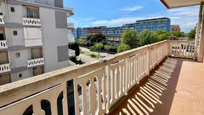 A balcony with a view of multi-story buildings, a clear sky, and a street with trees.