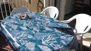 A round table with a blue tablecloth featuring white coral and seaweed patterns, surrounded by white chairs.