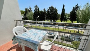 A balcony with a table and chairs, a view of a street and trees, and a metal railing. - Cozy flat with balcony-Beahost (Porto Santa Margherita)
