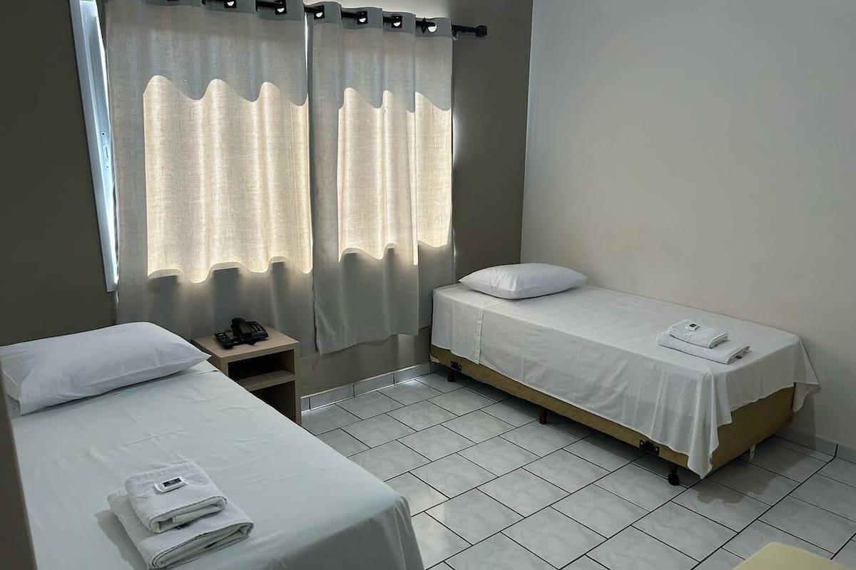 A hotel room with two single beds, a bedside table with a phone, and a window with curtains.