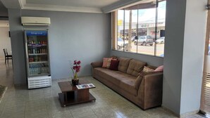 A reception area with a brown sofa, a small wooden table with a magazine, and a beverage vending machine. - Hotel Parati Arapongas (Arapongas)