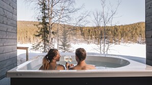 A couple in a hot tub with a snowy forest view. - Kurula's Resort (Pyhätunturi)
