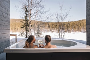 Una pareja en un jacuzzi con vistas a un bosque nevado.