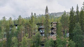 A multi-story building surrounded by dense forest and a lake. - Kurula's Resort (Pyhätunturi)