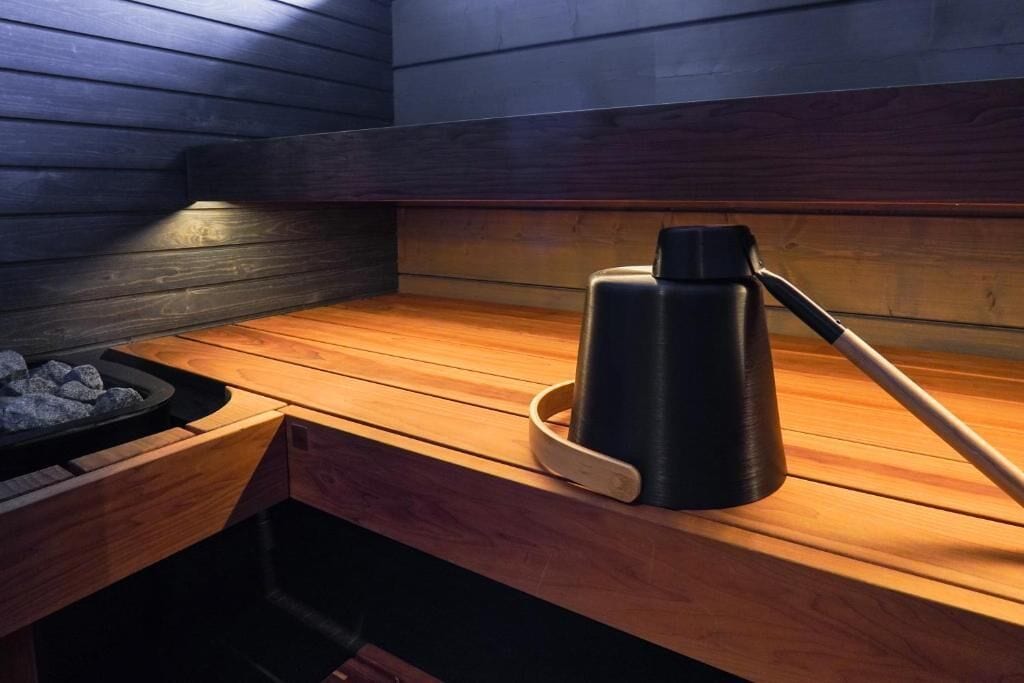 En sauna med træbænk, en sort vandbeholder og et varmeelement.