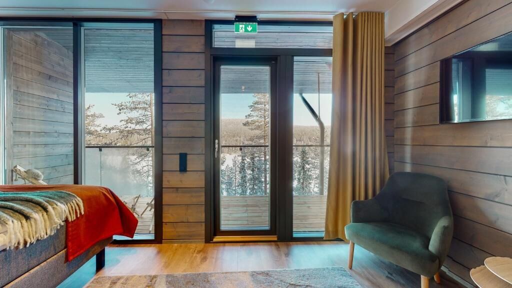 A room with a bed, a chair, a sliding glass door, and a view of trees.