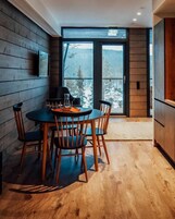 Un comedor con una mesa redonda y sillas, un televisor montado en la pared, y vista a un paisaje nevado a través de un ventanal grande.