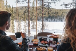 Una mesa de comedor con comida y bebidas, con vista a un paisaje nevado con árboles.