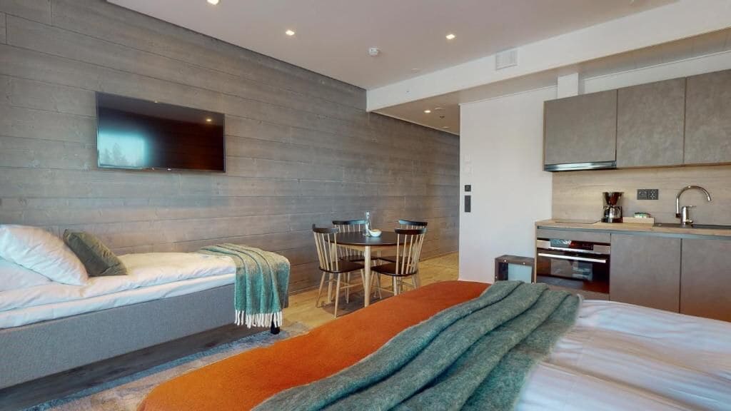 Una camera d'albergo moderna con un letto, un piccolo tavolo da pranzo, un divano, una TV a parete e un angolo cottura.