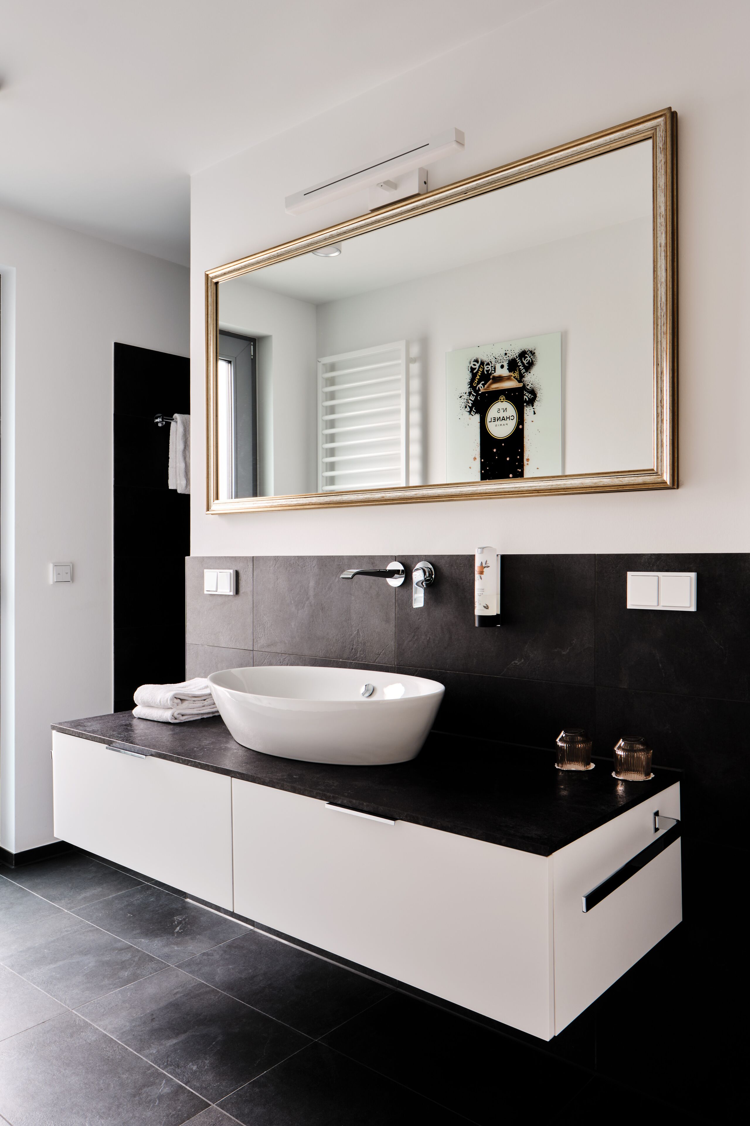 Un baño moderno con un espejo grande, un lavabo blanco de diseño y una encimera negra.