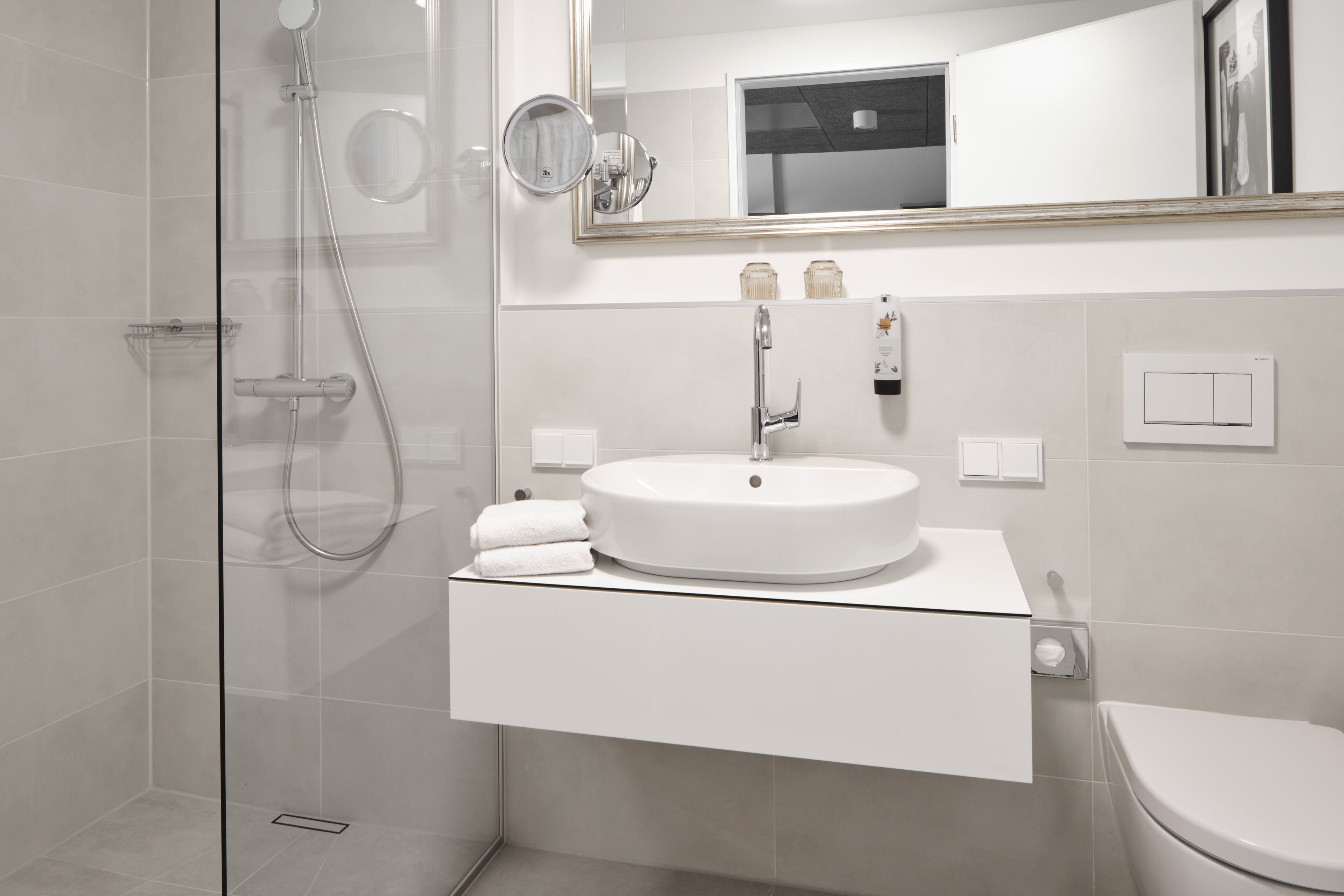 A modern bathroom with a glass shower enclosure, a white sink with a mirror above, and a toilet.