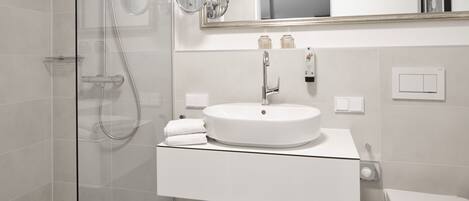 Une salle de bain moderne avec une douche à parois de verre, un lavabo blanc avec un miroir au-dessus et des toilettes.
