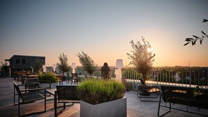 Une terrasse sur le toit avec des sièges extérieurs, un jardinier avec des plantes et une vue sur le coucher du soleil.