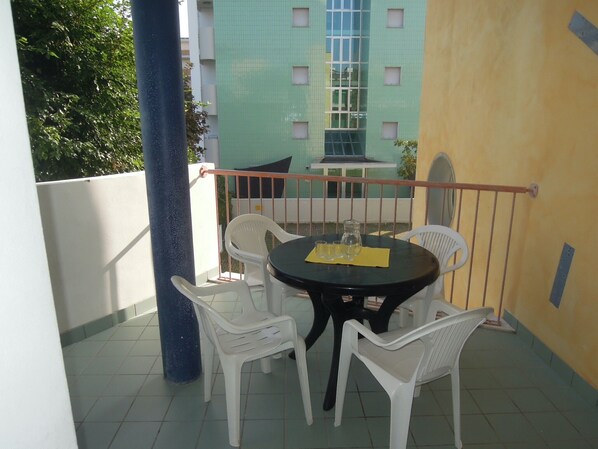 Een klein balkon met een ronde tafel en vier witte plastic stoelen.