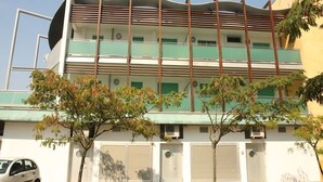 Un edificio de varios pisos con techo plano y balcones, con un coche estacionado frente a él.