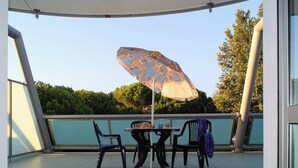 Un área de estar al aire libre con techo, una mesa, sillas, un paraguas y vistas a árboles y edificios al fondo.