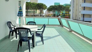 Un balcón con una mesa y sillas, un reloj y vistas a edificios y árboles.