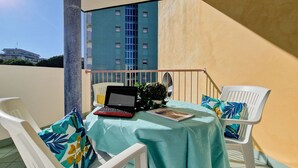 En balkon med et bord, to hvide stole, en bærbar computer og en potteplante.