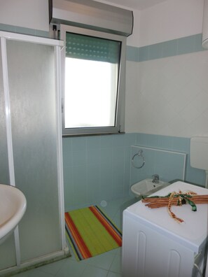 Een badkamer met toilet, wastafel, raam met deur van geëtste glas en een kleurrijk gestreept vloerkleed.