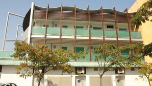 A multi-story building with a flat roof and a series of balconies. There are trees in front of the building, and a car parked on the left side. - Cozy apartment 200 m from the beach (Bibione)