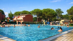 A swimming pool with people in it, surrounded by buildings and trees. - Modern apartment with swimming pools - Beahost (Bibione)