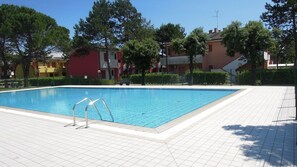 A swimming pool with a tiled deck, surrounded by trees and buildings.