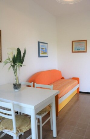 Una habitación con una mesa blanca, una silla naranja, una cama con cabecera naranja y un cuadro en la pared.