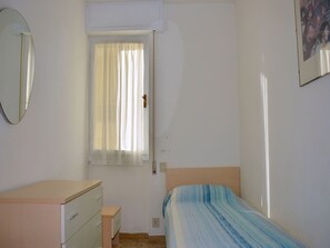 Une chambre à coucher avec un lit, une commode, une fenêtre avec des rideaux, un miroir et un tableau accroché au mur.