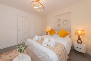 A hotel room with a bed, two bedside lamps, a small bedside table, and a door. - Modern 2bedroom Flat Freeparking (Reading)