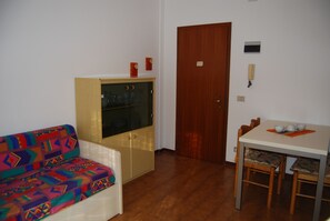 Una habitación con sofá, un armario, una puerta de madera, una mesa con sillas y una ventana pequeña.