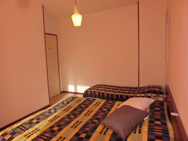 A small, narrow room with a single bed and a hanging light fixture.