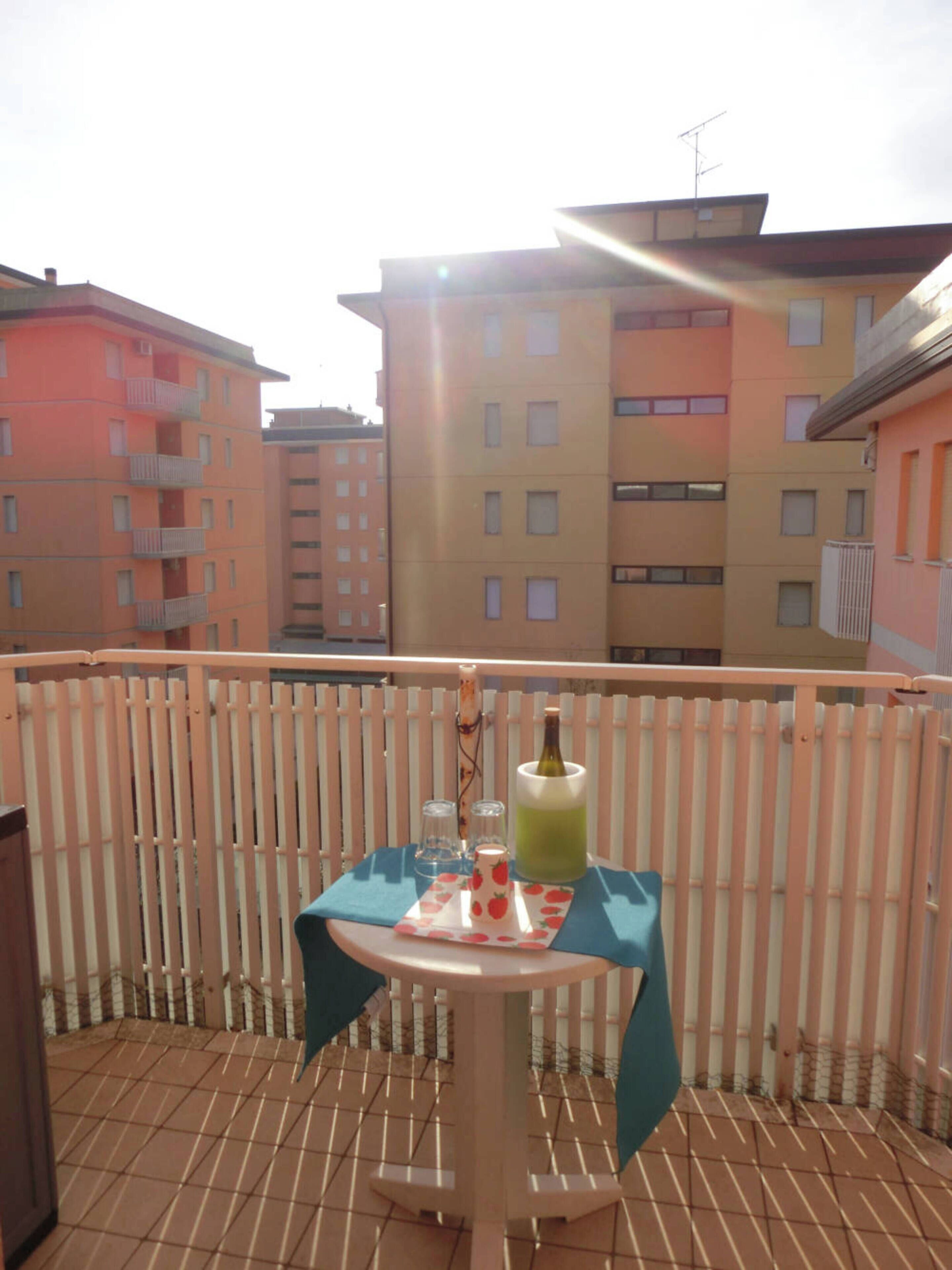 A balcony with a table set for two, a bottle of drink, and a small vase.