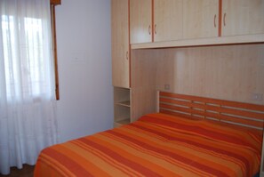 Ein Schlafzimmer mit Bett, Holzschrank und einem Fenster mit Vorhängen.