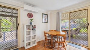 A dining area with a wooden table and chairs, a white bookshelf, and a wall clock. - Safety Beach Cottage (Safety Beach)