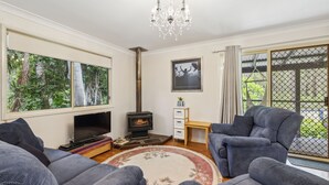 A living room with a fireplace, a TV, and a large window with a view of trees. - Safety Beach Cottage (Safety Beach)