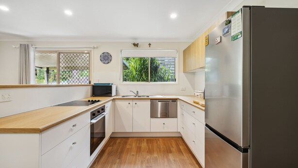 A modern kitchen with white cabinets, a stainless steel refrigerator, a built-in oven, and a window with a view of greenery. - Safety Beach Cottage (Safety Beach)