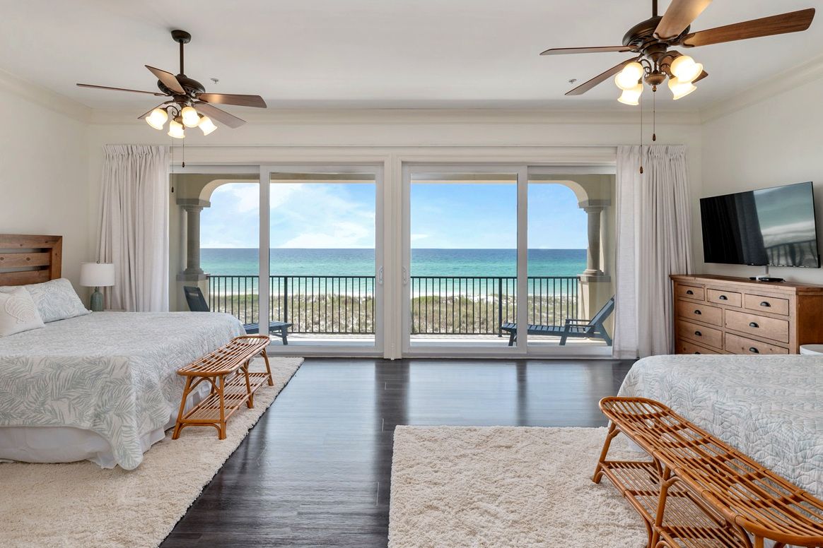 A bedroom with two beds, a TV, and a balcony with a view of the ocean.