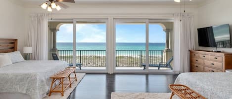 A bedroom with two beds, a TV, and a balcony with a view of the ocean.