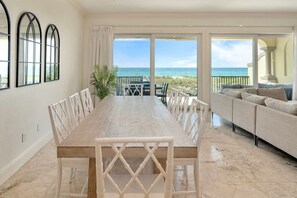 A dining area with a long table and chairs, a sofa, and a view of the ocean. - 6 Bedroom | 7 King Beds | Elevator | Beachfront (Navarre)