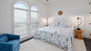 A bedroom with a large bed, two windows with blinds, a blue chair, and a nightstand with a lamp. - 6 Bedroom | 7 King Beds | Elevator | Beachfront (Navarre)