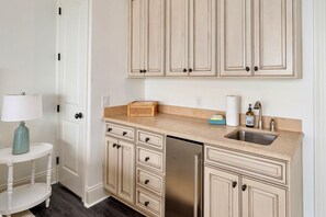 A kitchen with white cabinetry, a stainless steel dishwasher, a sink, and a small table with a lamp. - 6 Bedroom | 7 King Beds | Elevator | Beachfront (Navarre)
